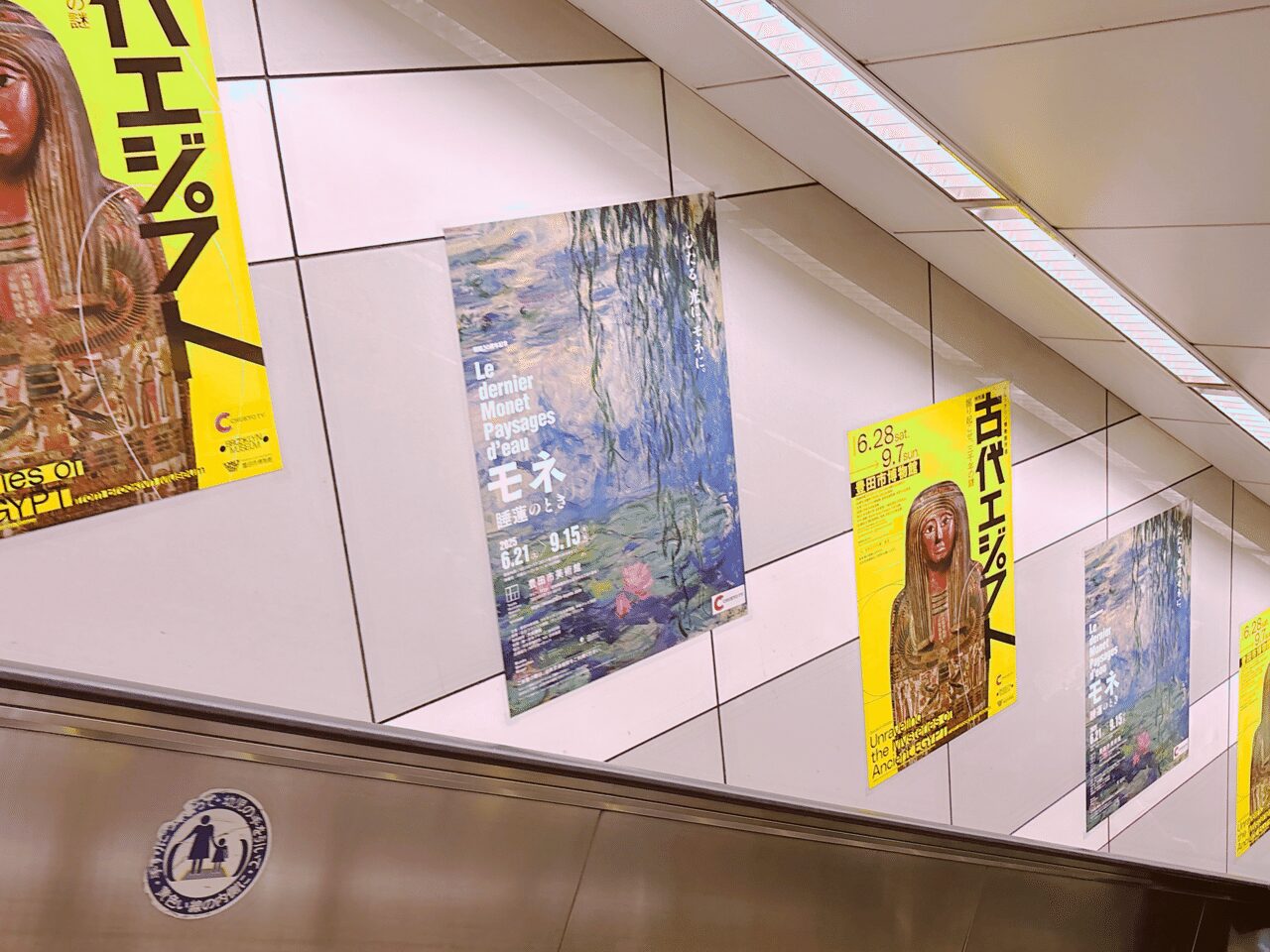エスカレーターの壁に貼られている美術館の催しものの2種類のポスター
