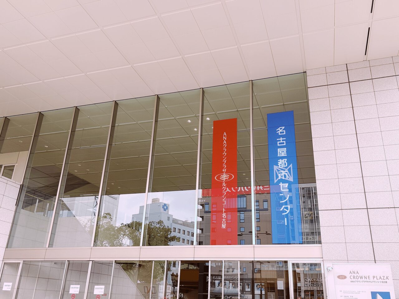 金山南ビルの出入り口、ANAクラウンプラザホテルグランコート名古屋の文字の垂れ幕と、名古屋都市センターの文字の垂れ幕。自動ドアの上は2階部分くらいまでガラス張り。