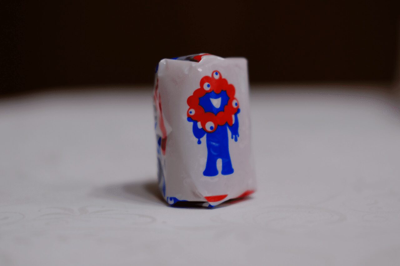 親指ほどの小さなお菓子がミャクミャクのデザインに包まれている。テーブルの上にそれを立たせて撮影した画像